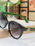 Gucci side view sunglasses with black round frame, green temple text, gold hinge emblem.