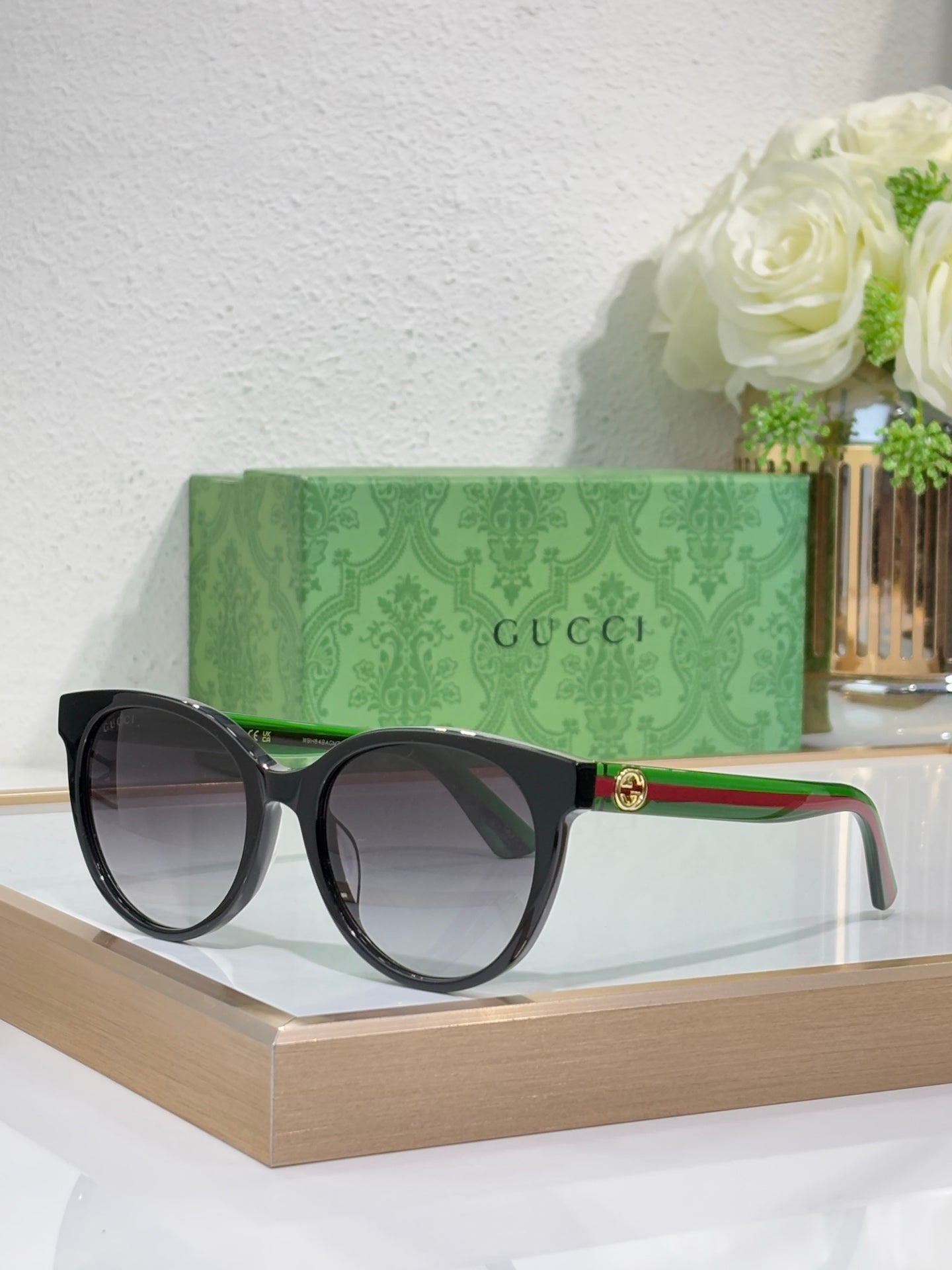 Gucci black round sunglasses with dark lenses, green temple stripe and gold logo detail.