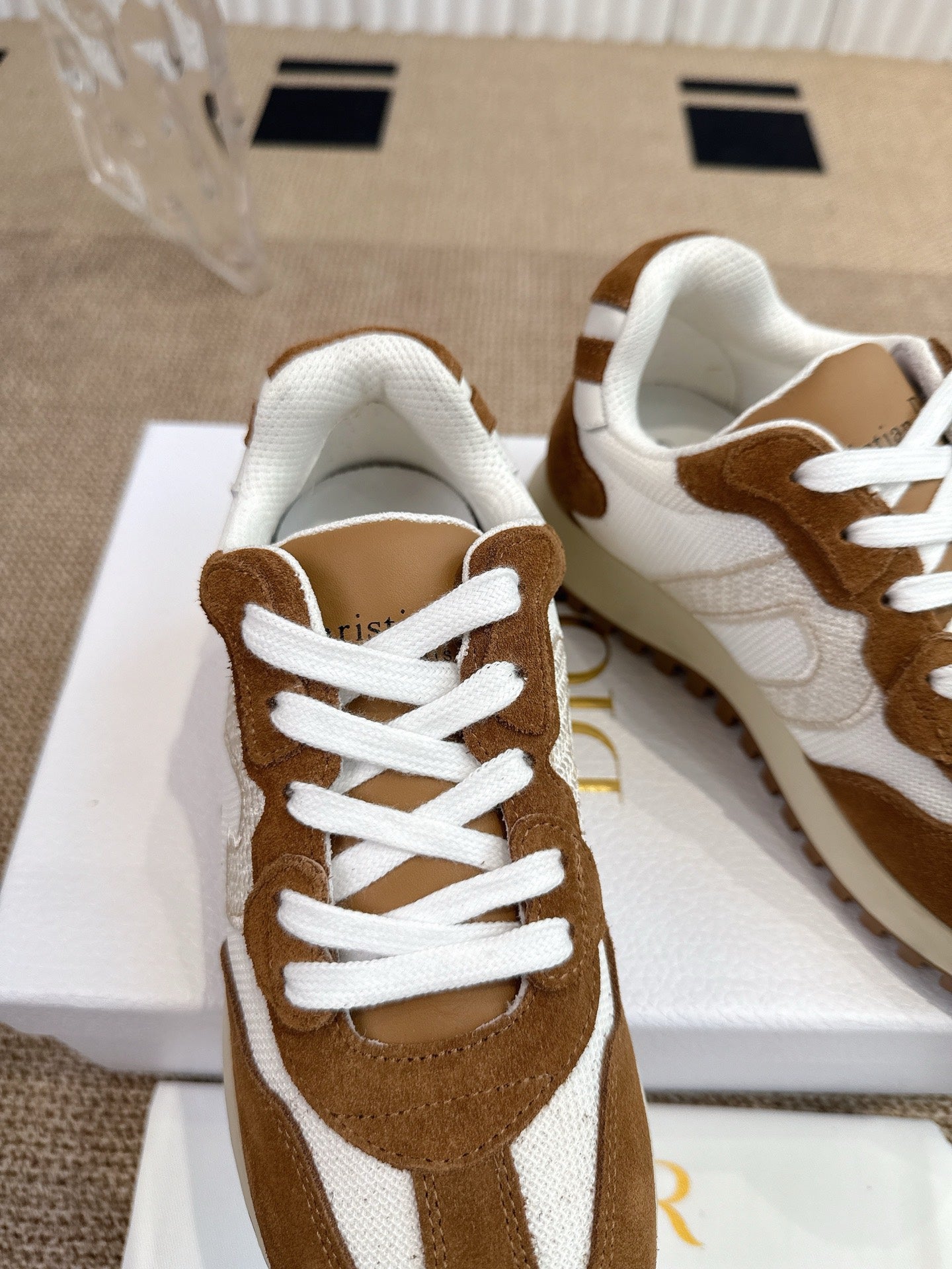 Dior unisex sneakers close-up, brown suede with white panels and lace eyelets.