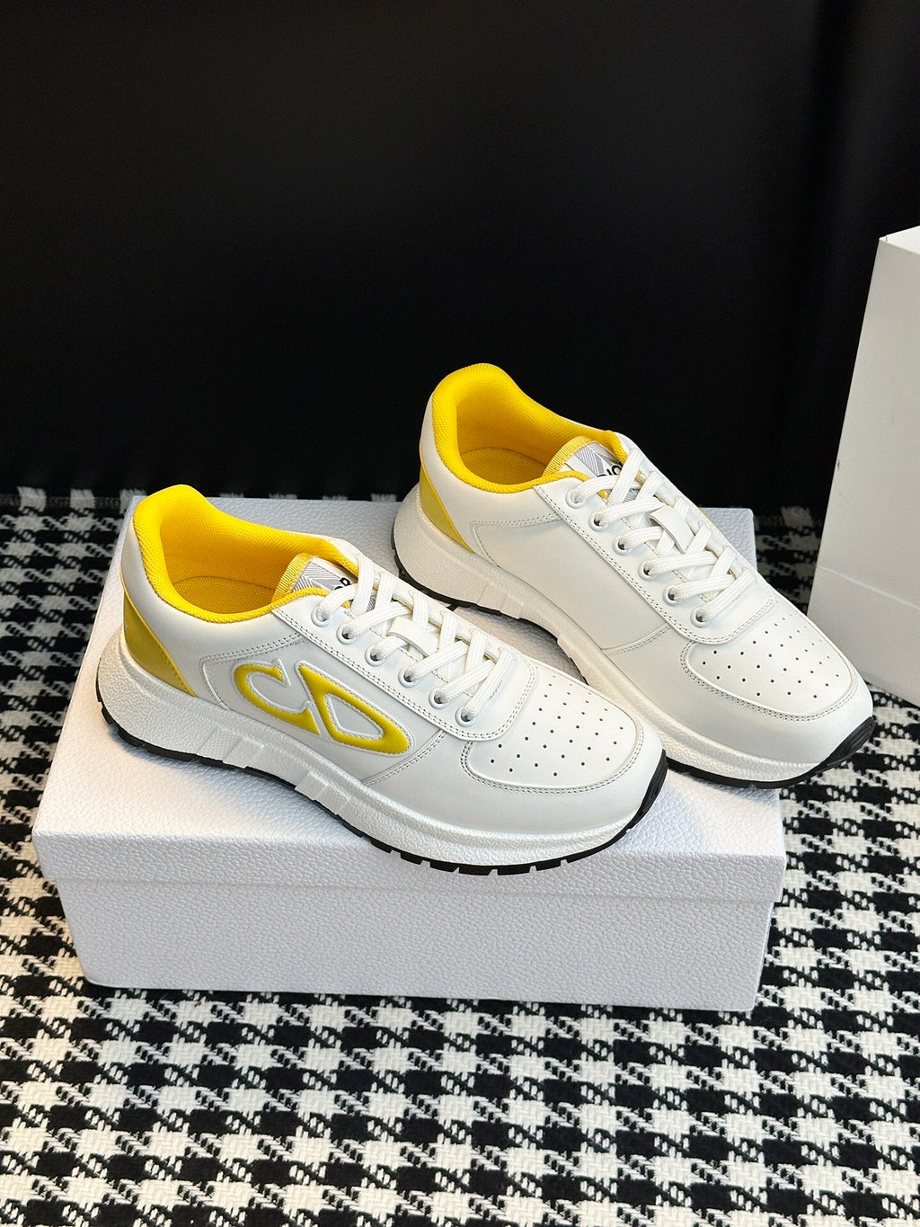 White low-top sneakers with yellow logo accents, perforated toe, and lace-up front