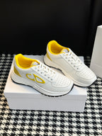 White low-top sneakers with yellow logo accents, perforated toe, and lace-up front