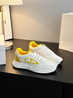 White low-top sneakers with yellow side emblem, perforated detailing, and thick sole