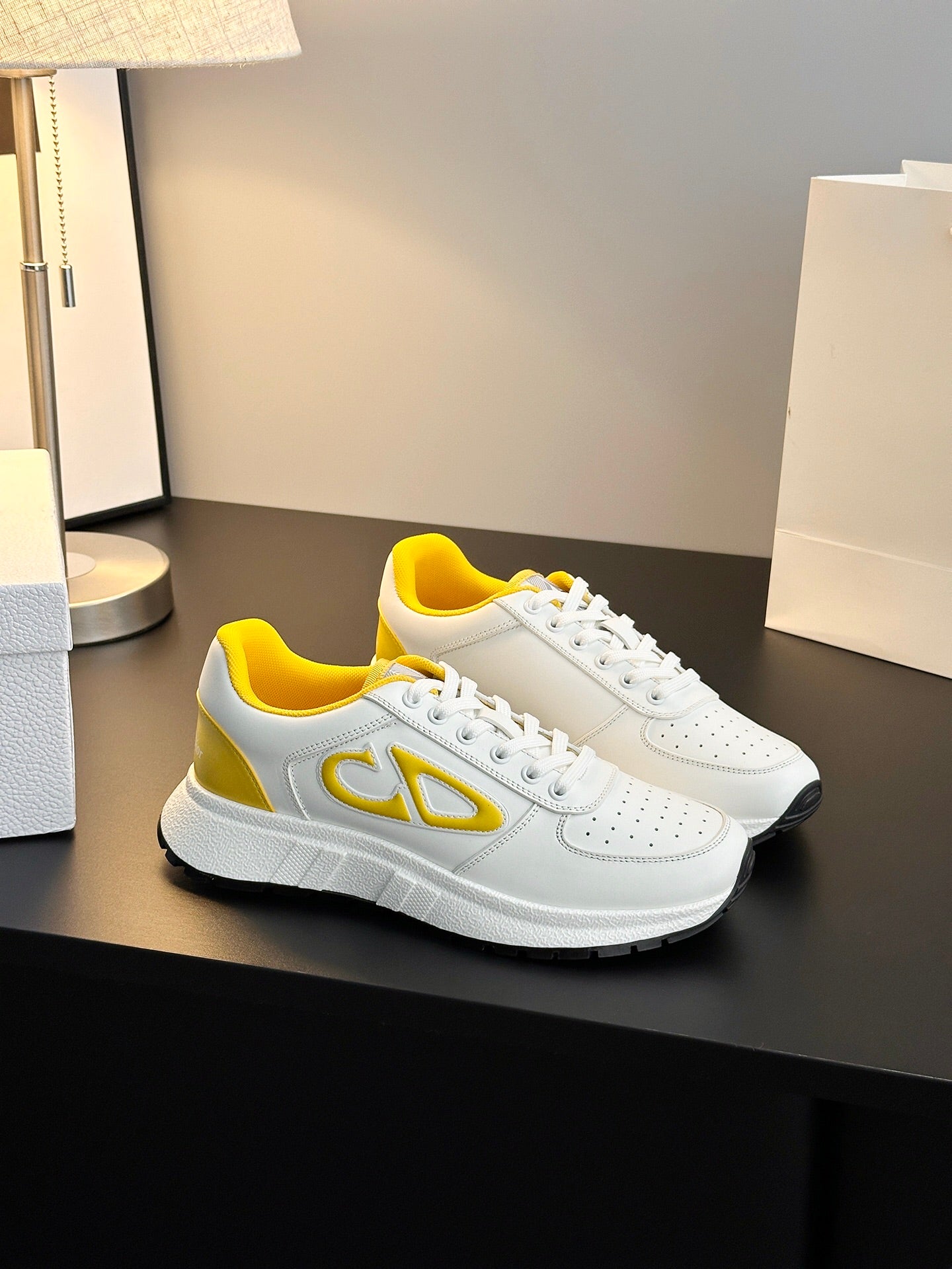 White low-top sneakers with yellow side emblem, perforated detailing, and thick sole