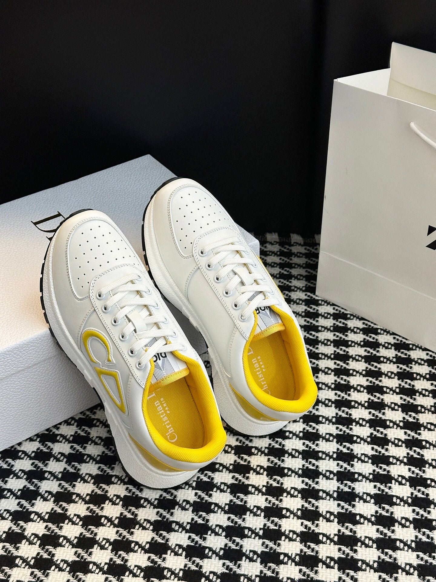 White low-top sneakers with yellow-trimmed heel and gold-toned side logo