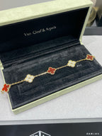 Gold-tone clover motif bracelet with red enamel on black jewelry display