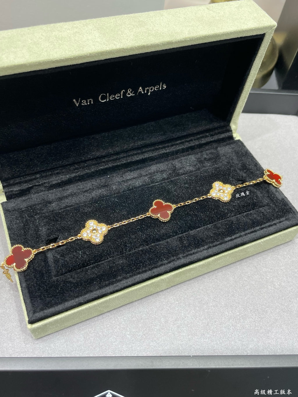 Gold-tone clover bracelet with red enamel and pavé links on velvet tray