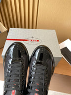Prada black lace-up sneakers close-up with red logo label and glossy front panels.