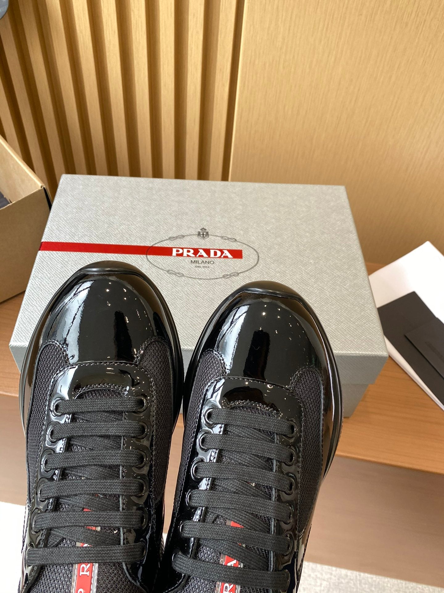 Prada black lace-up sneakers close-up with red logo label and glossy front panels.