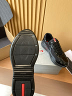 Black sneaker outsole with tread and Prada branding, shown with matching pair on box.