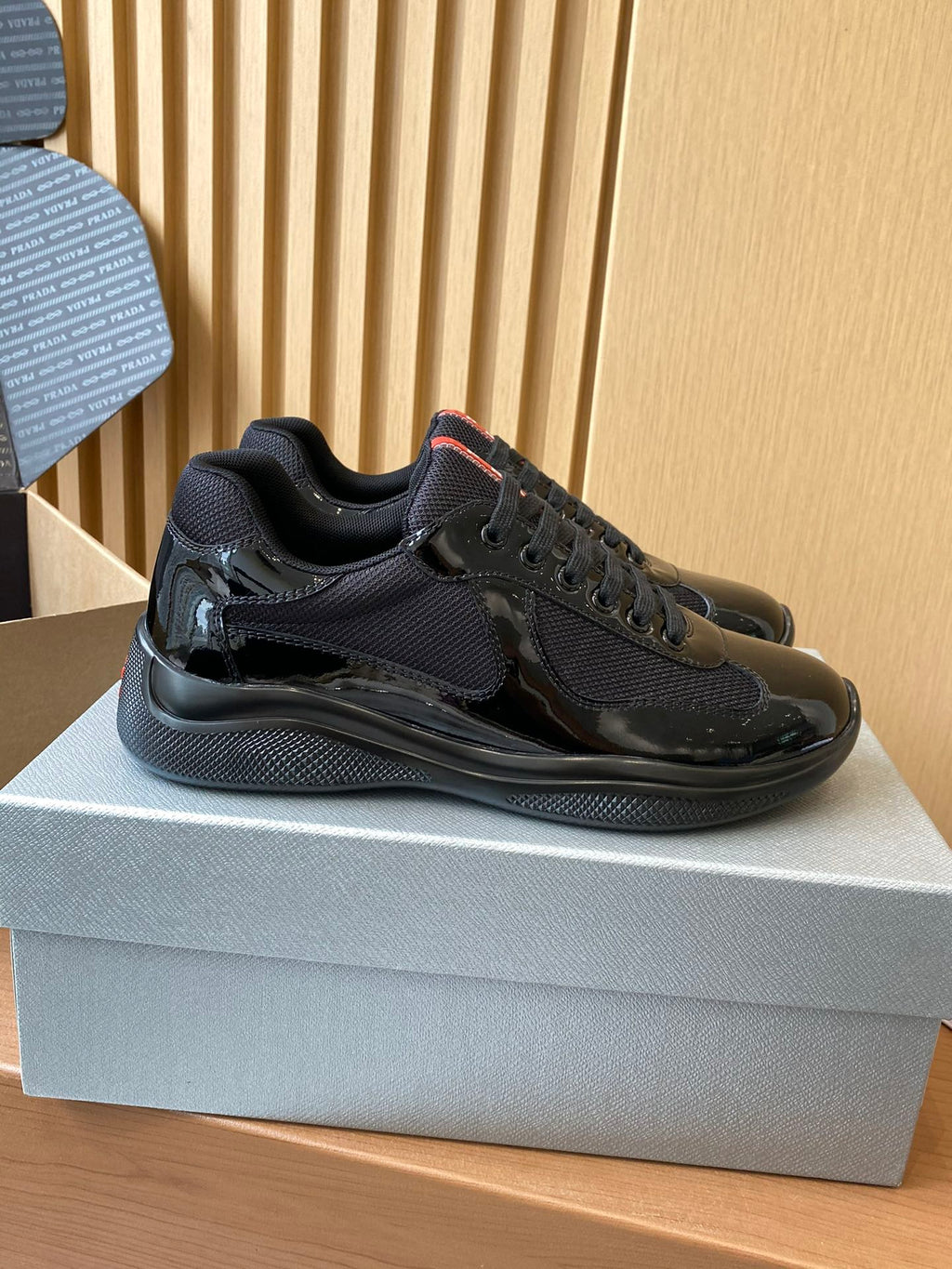 Black lace-up sneakers with textured panels and chunky sole, side view on shoe box.