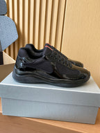 Black lace-up sneakers with textured panels and chunky sole, side view on shoe box.
