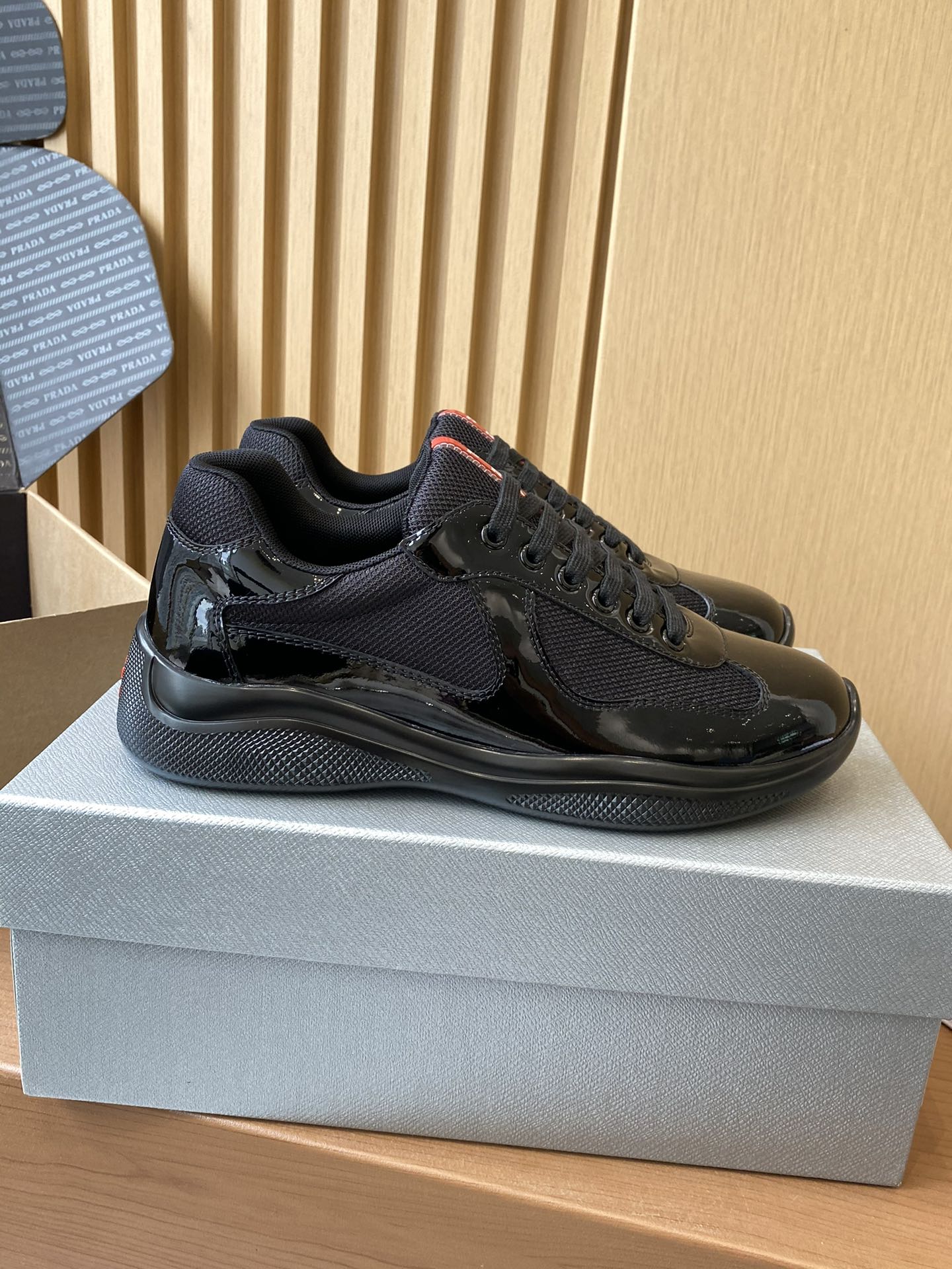 Black lace-up sneakers with textured panels and chunky sole, side view on shoe box.
