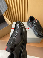 Black Prada lace-up sneakers with perforated side panels and red logo tab, on box.