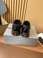 Black Prada sneakers with red heel tabs, rear view on shoe box.
