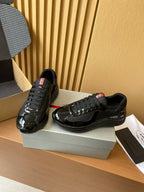 Black lace-up sneakers with glossy finish and red heel labels, standing on shoe box.