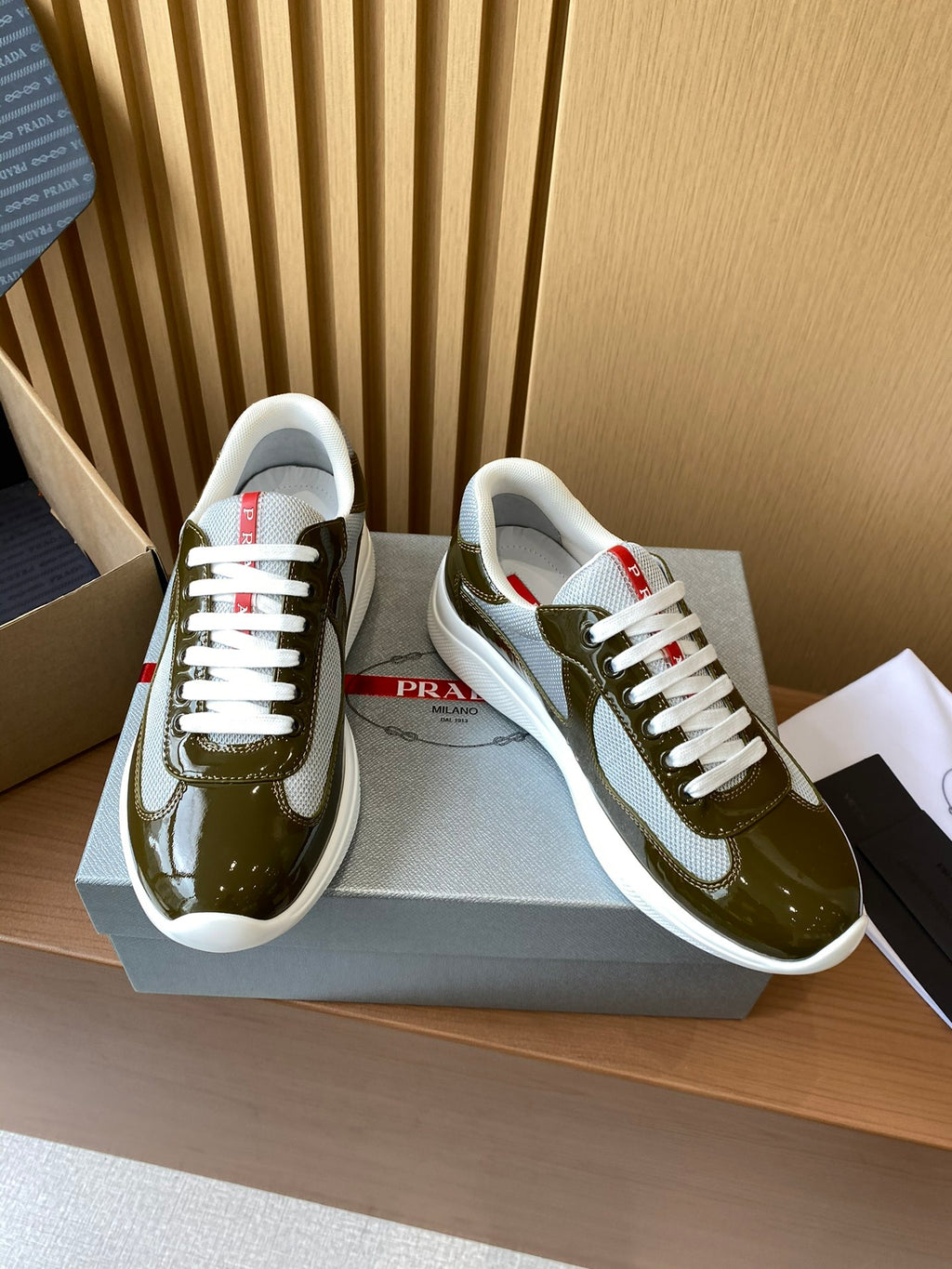 Prada unisex sneakers on box, olive green patent leather with white laces
