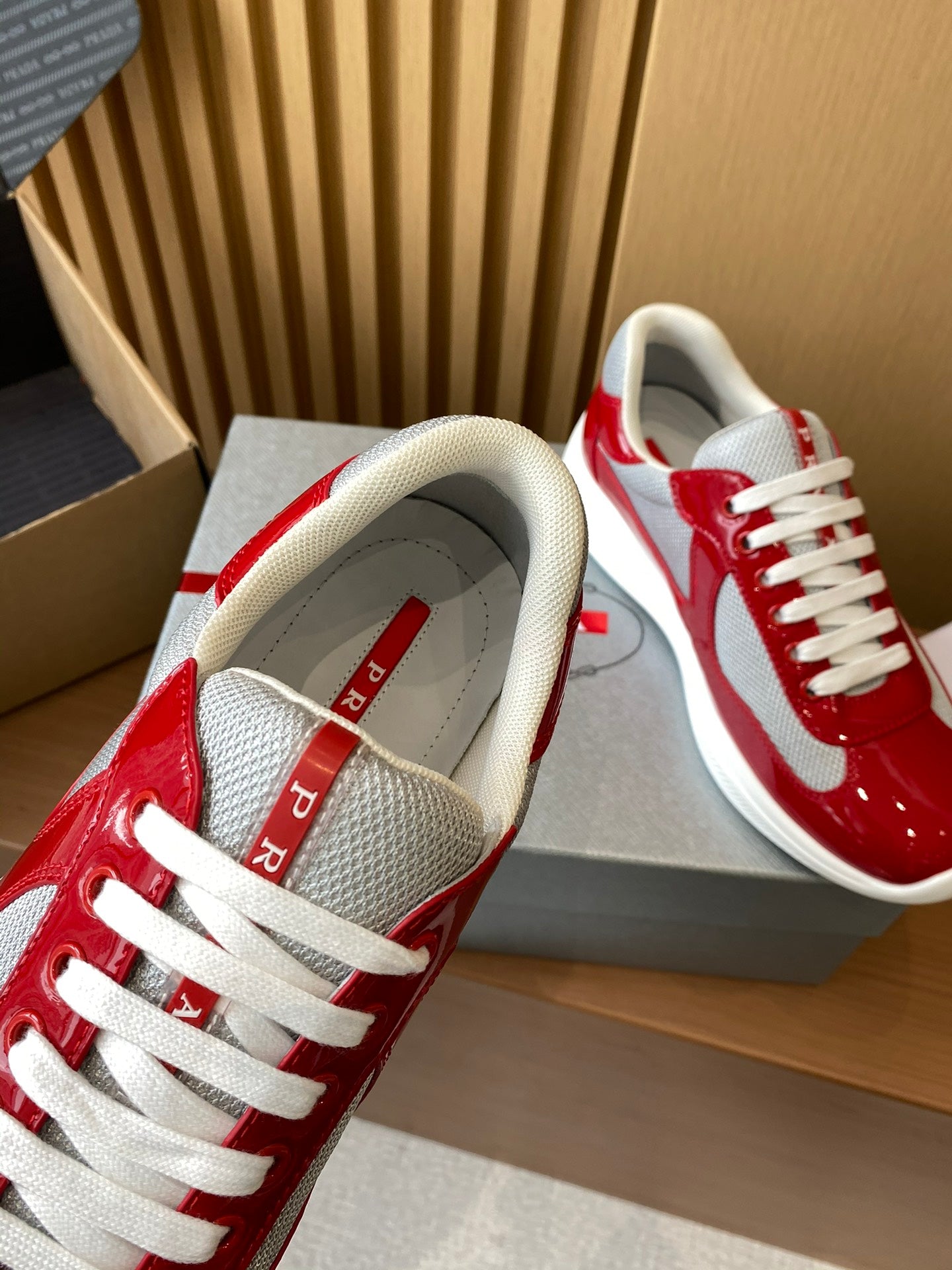 Prada unisex sneakers with red heel, white lining, and lace-up design on box