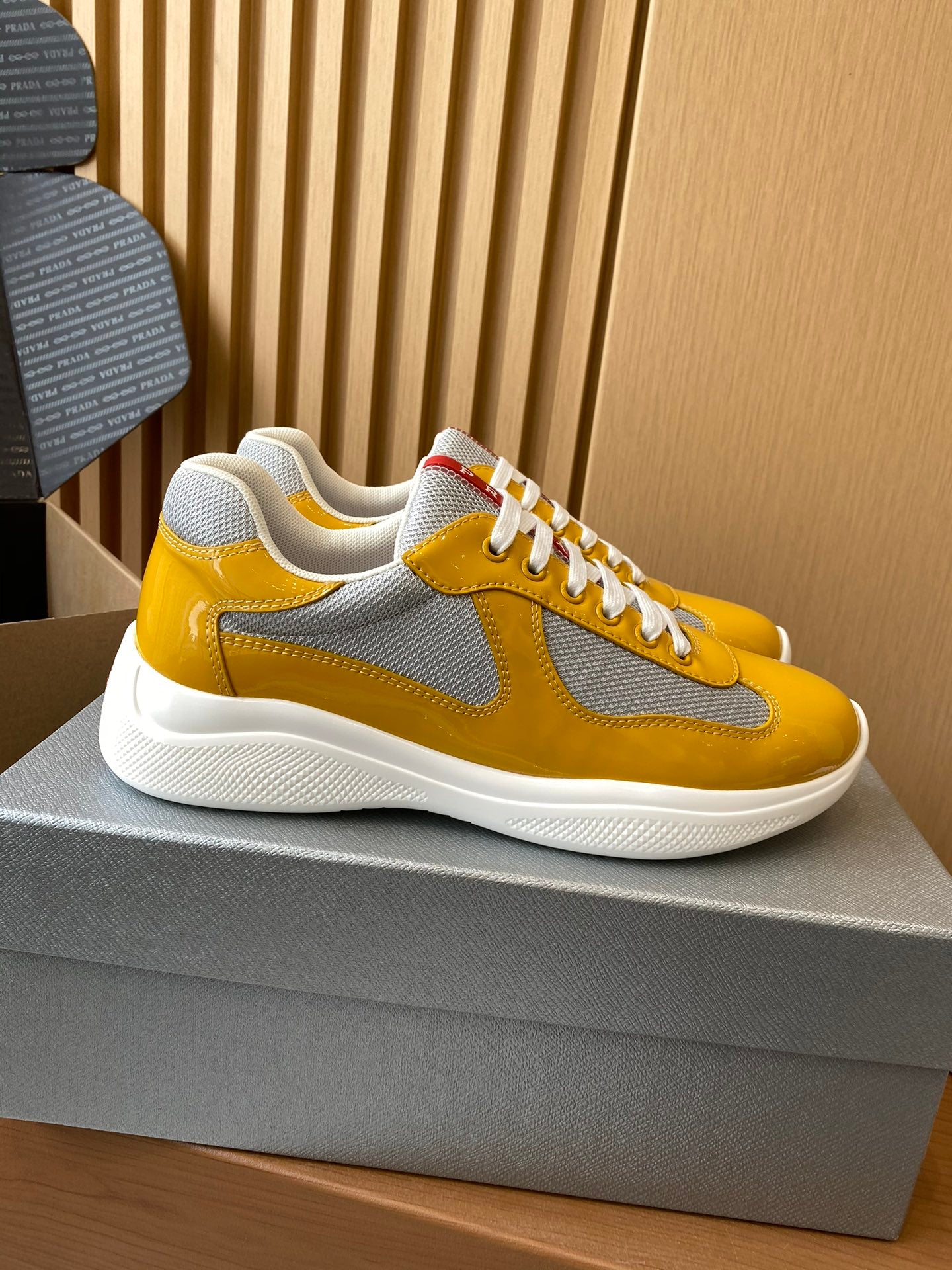 Prada unisex sneakers on box, yellow suede and patent with gray swoosh detail