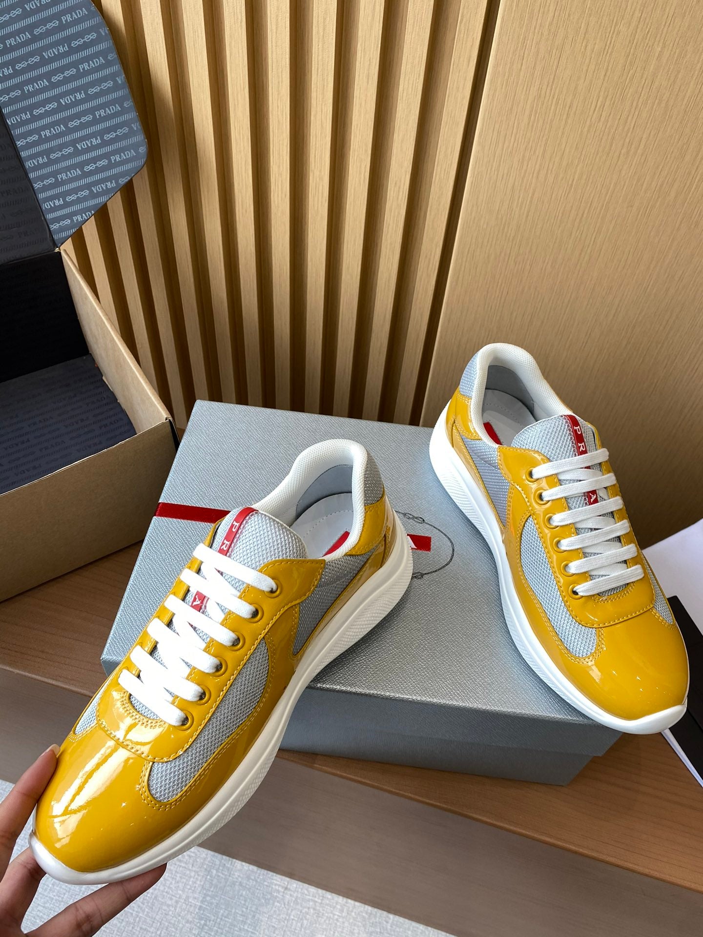 Prada unisex sneakers close-up, yellow patent toe with white laces and red tab
