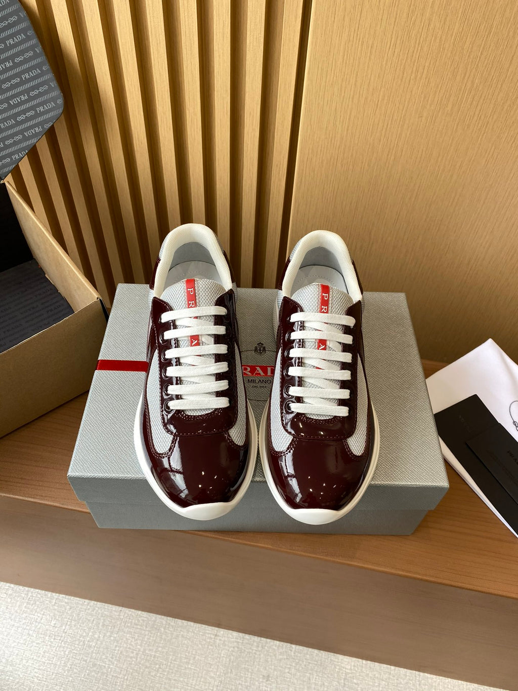 Burgundy low-top sneakers with white laces and white rubber sole, red logo accents