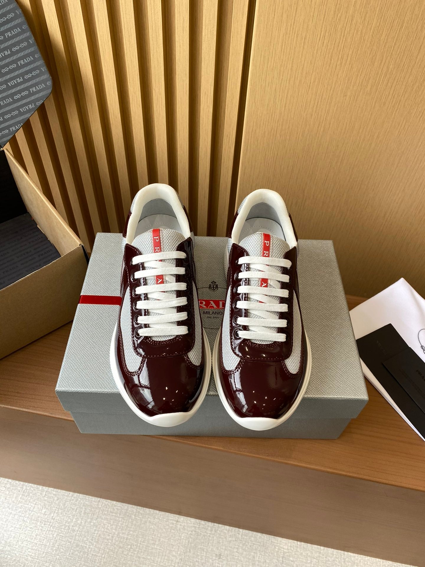 Burgundy low-top sneakers with white laces and white rubber sole, red logo accents