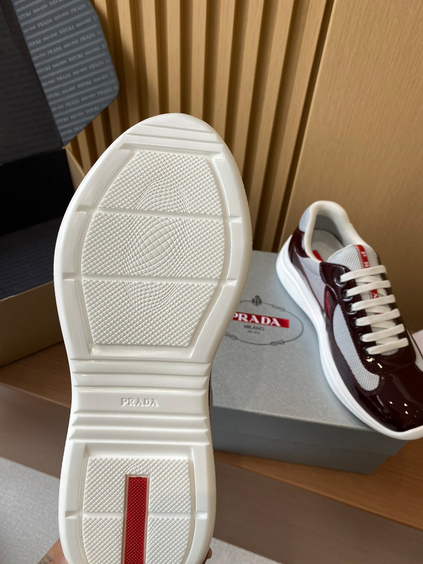 Outsole view of white sneaker with burgundy upper and red logo accent on heel
