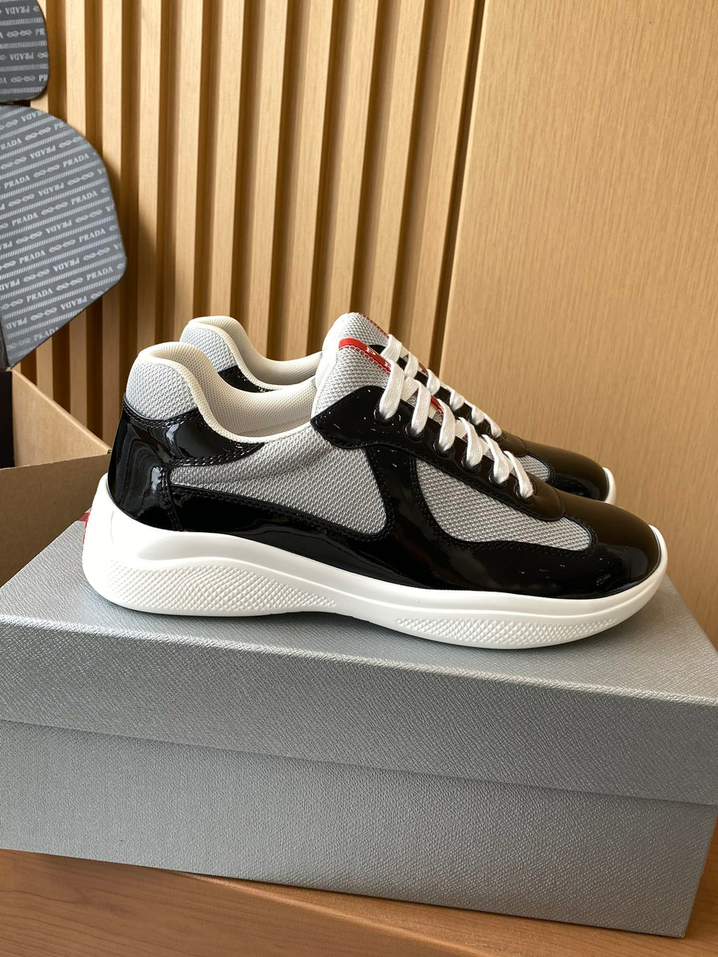 Prada unisex sneakers side view, black patent with grey swoosh, white laces