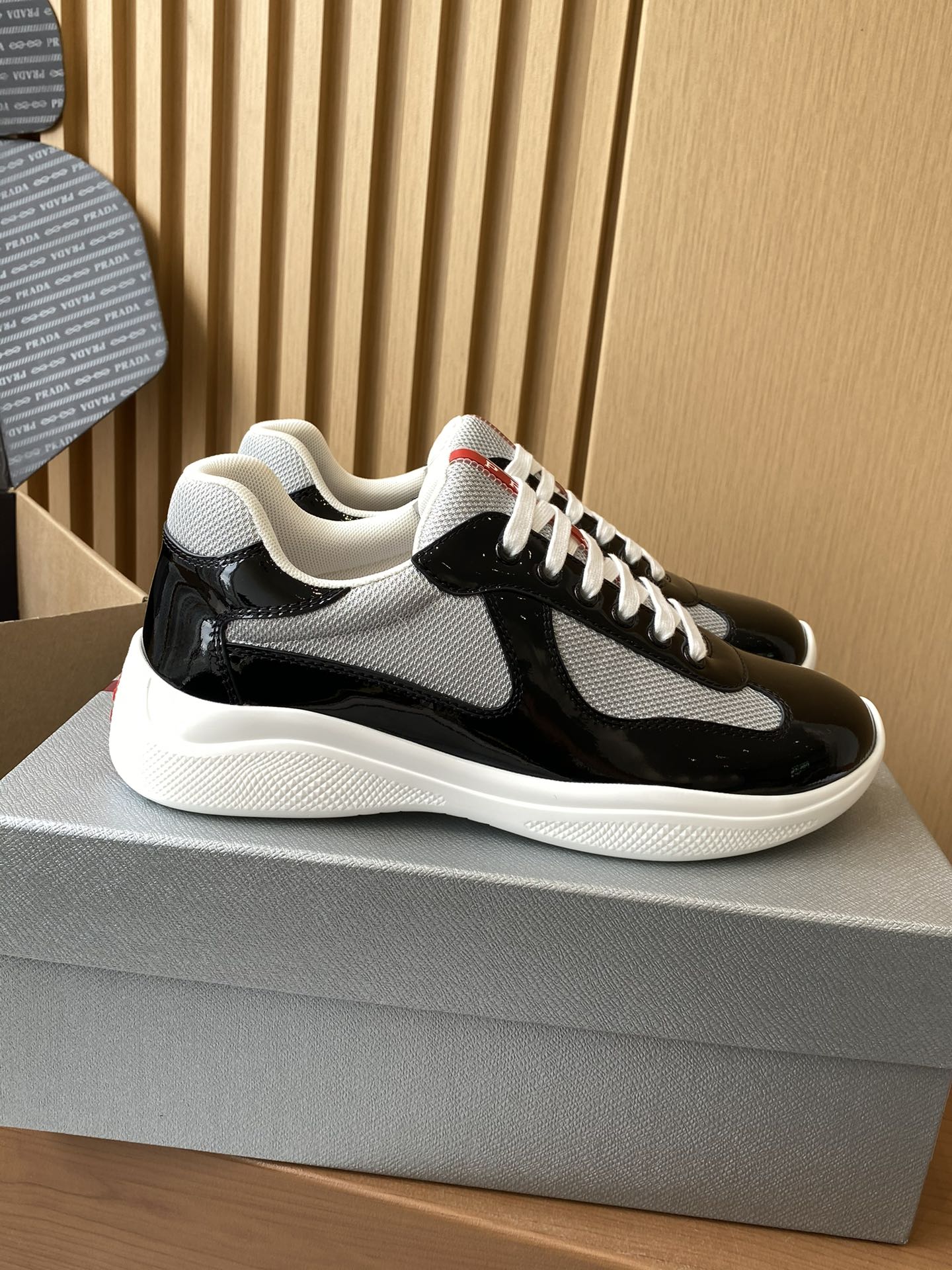 Prada unisex sneakers side view, black patent with grey swoosh, white laces
