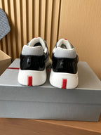 Prada unisex sneakers back view, black patent with red heel tabs and white soles