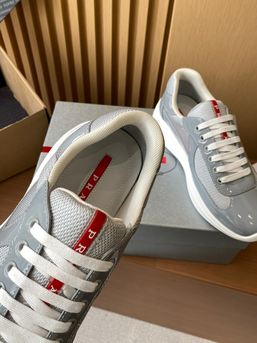 Unisex sneakers with light gray uppers, white laces, and red logo text on the tongue