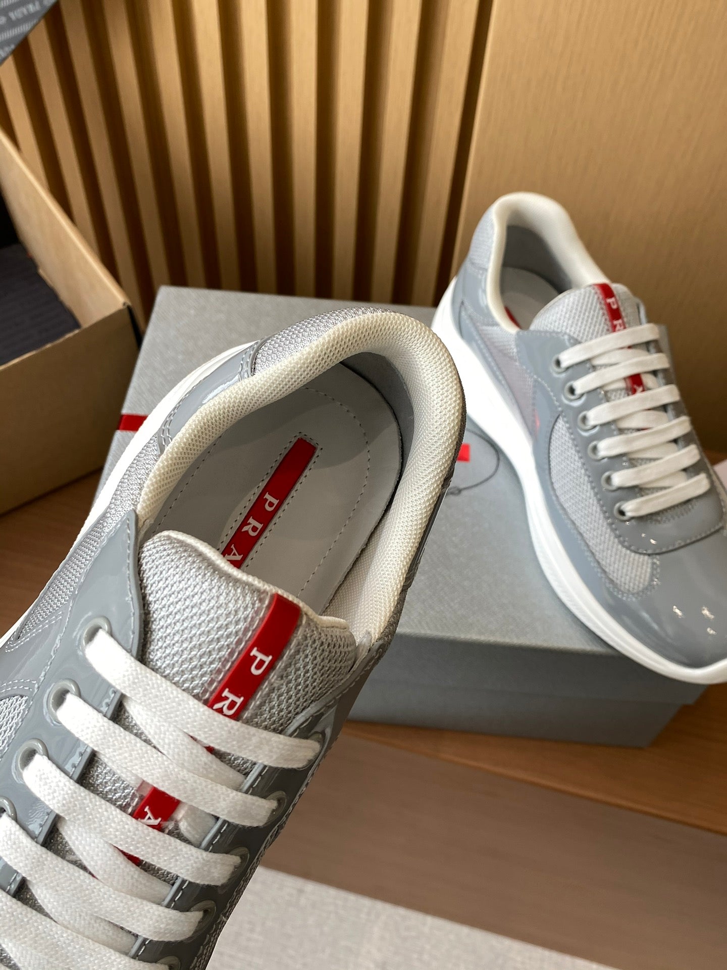 Unisex sneakers with light gray uppers, white laces, and red logo text on the tongue