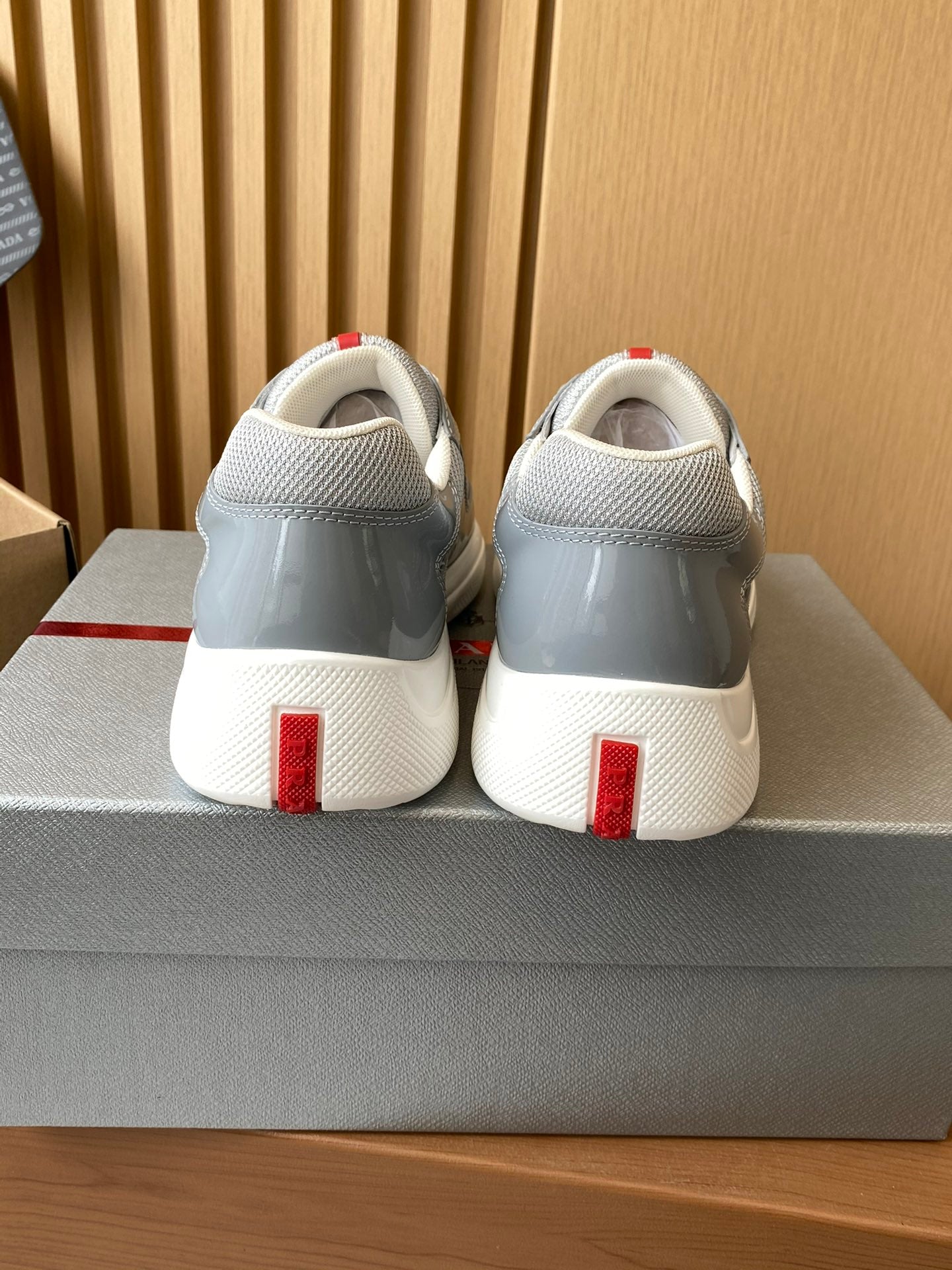 Light gray unisex sneakers from the back with white laces, red heel accents, on a box