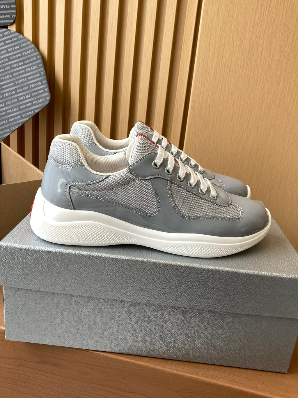 Light gray unisex lace-up sneakers with textured panels, white midsoles, and red accents