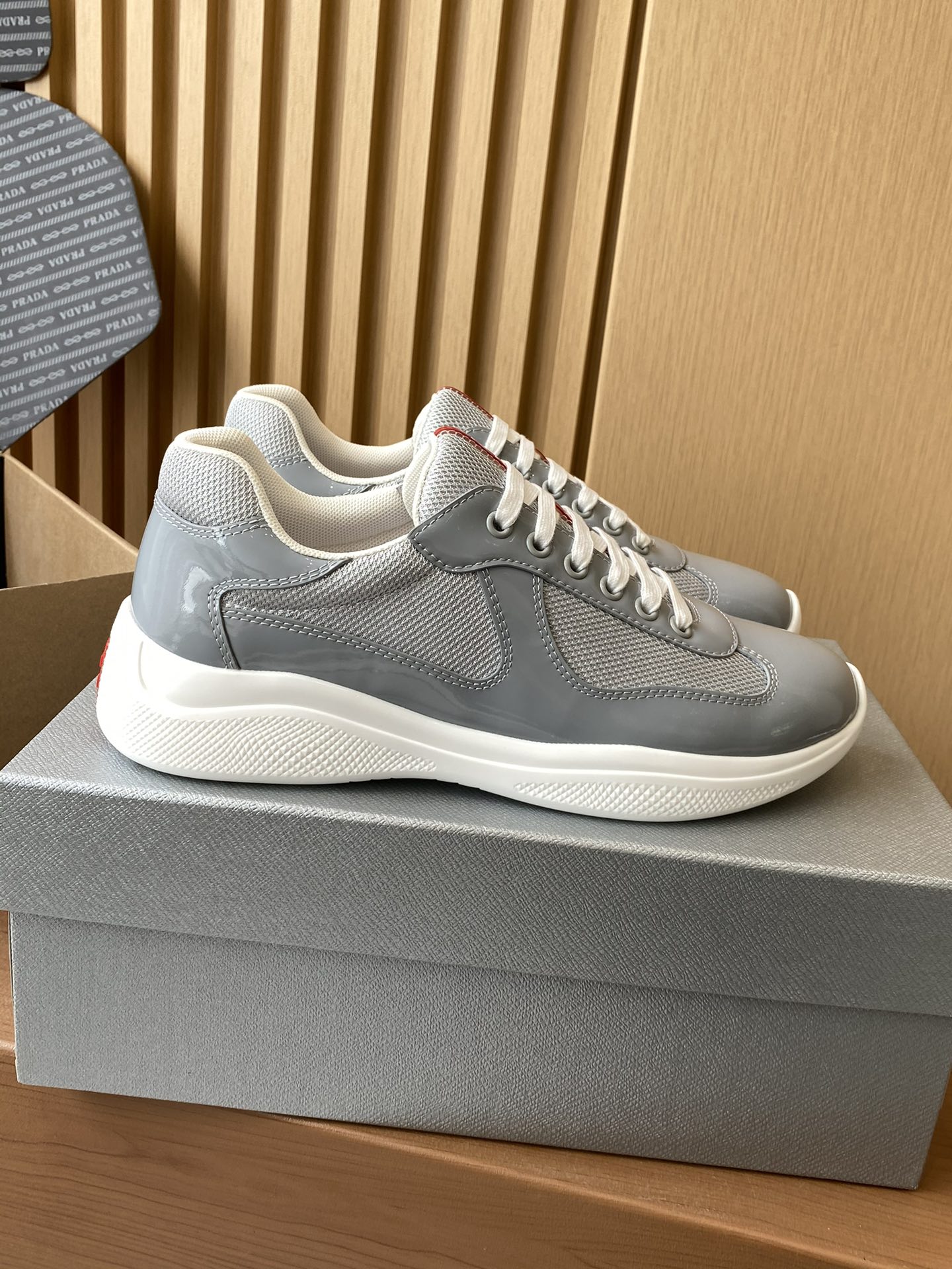 Light gray unisex lace-up sneakers with textured panels, white midsoles, and red accents