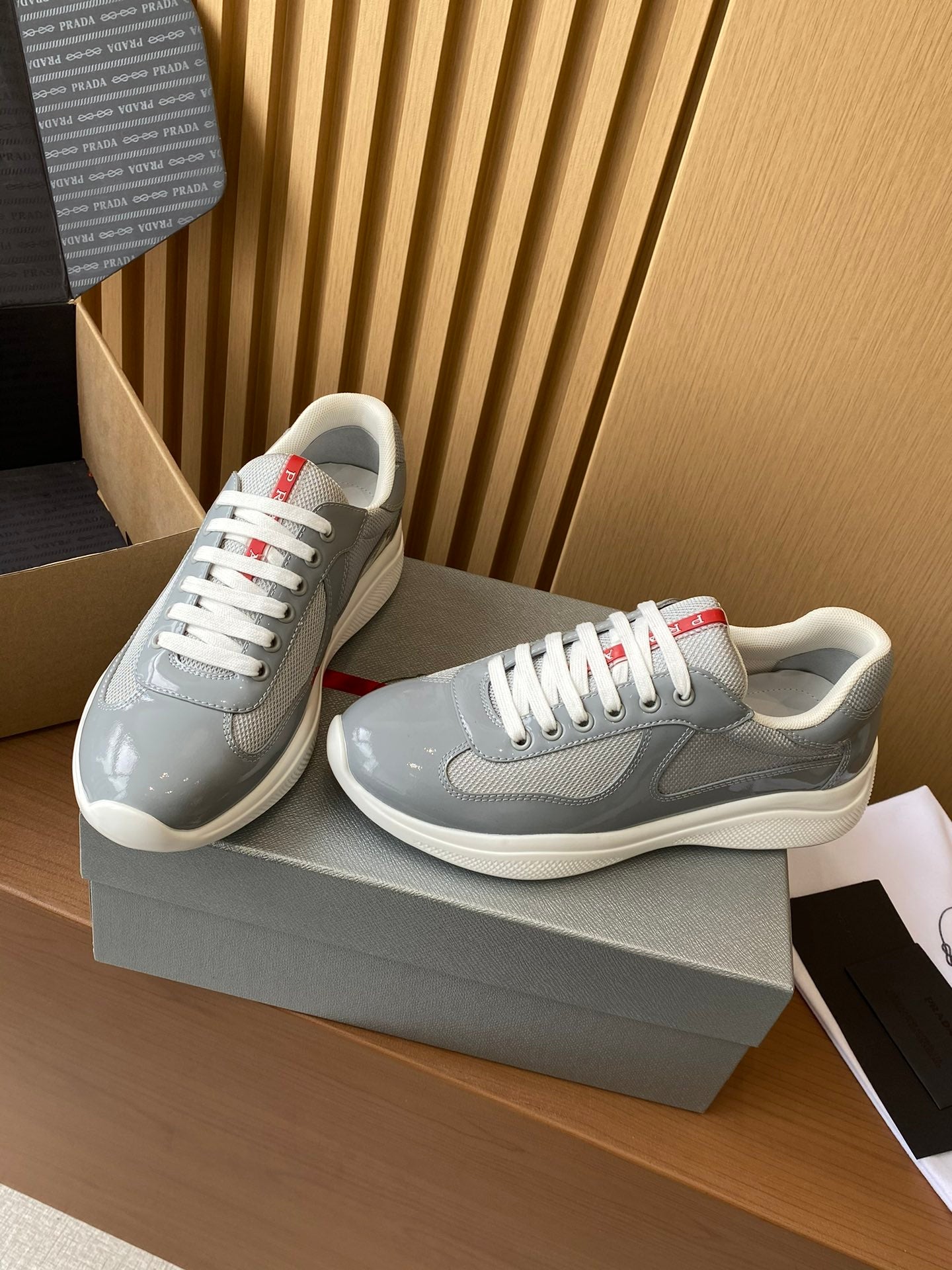 Light gray unisex sneakers with white laces and red heel/stripe accents, angled side view