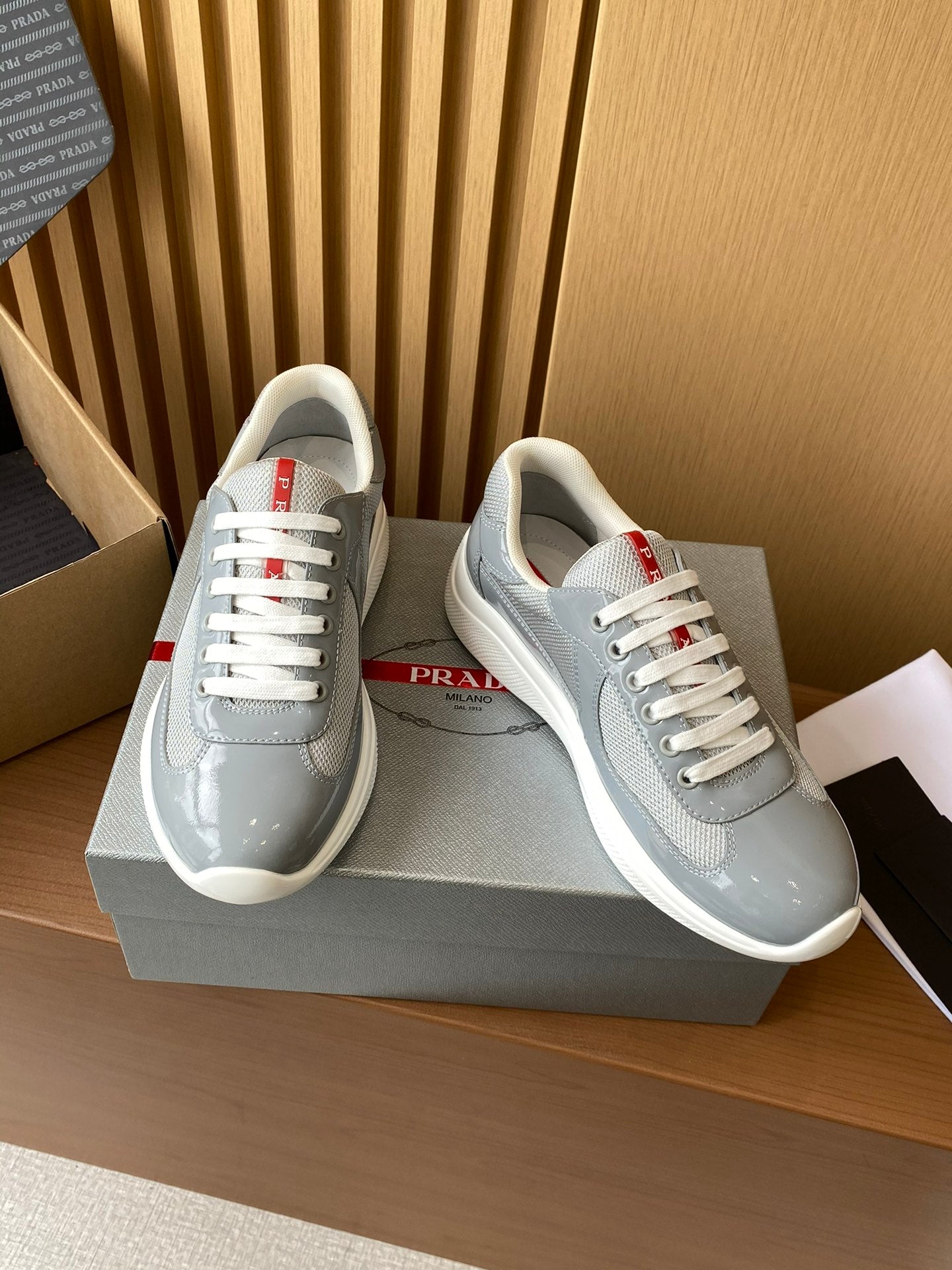 Pair of light gray unisex sneakers with white laces and red logo details, side view