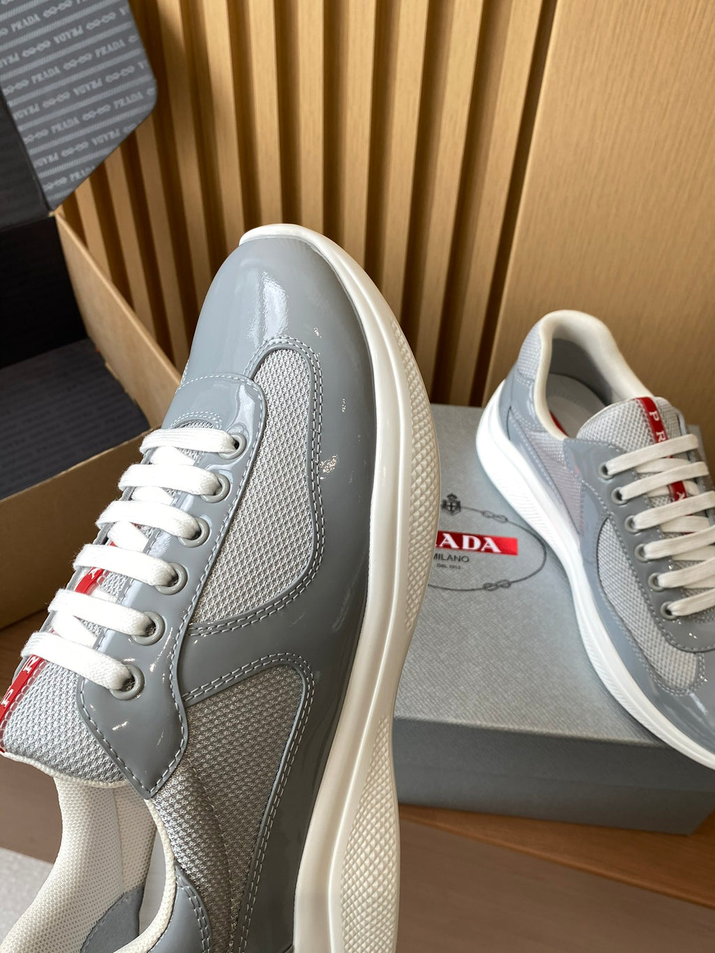 Light gray unisex sneakers shown from the side with white laces and red label detail