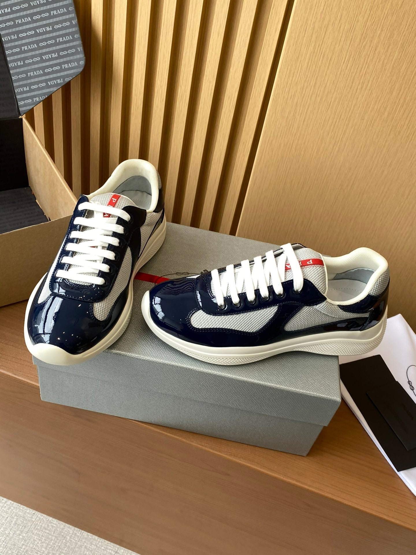 Prada navy and white low-top sneakers on a box, lace-up front and side view