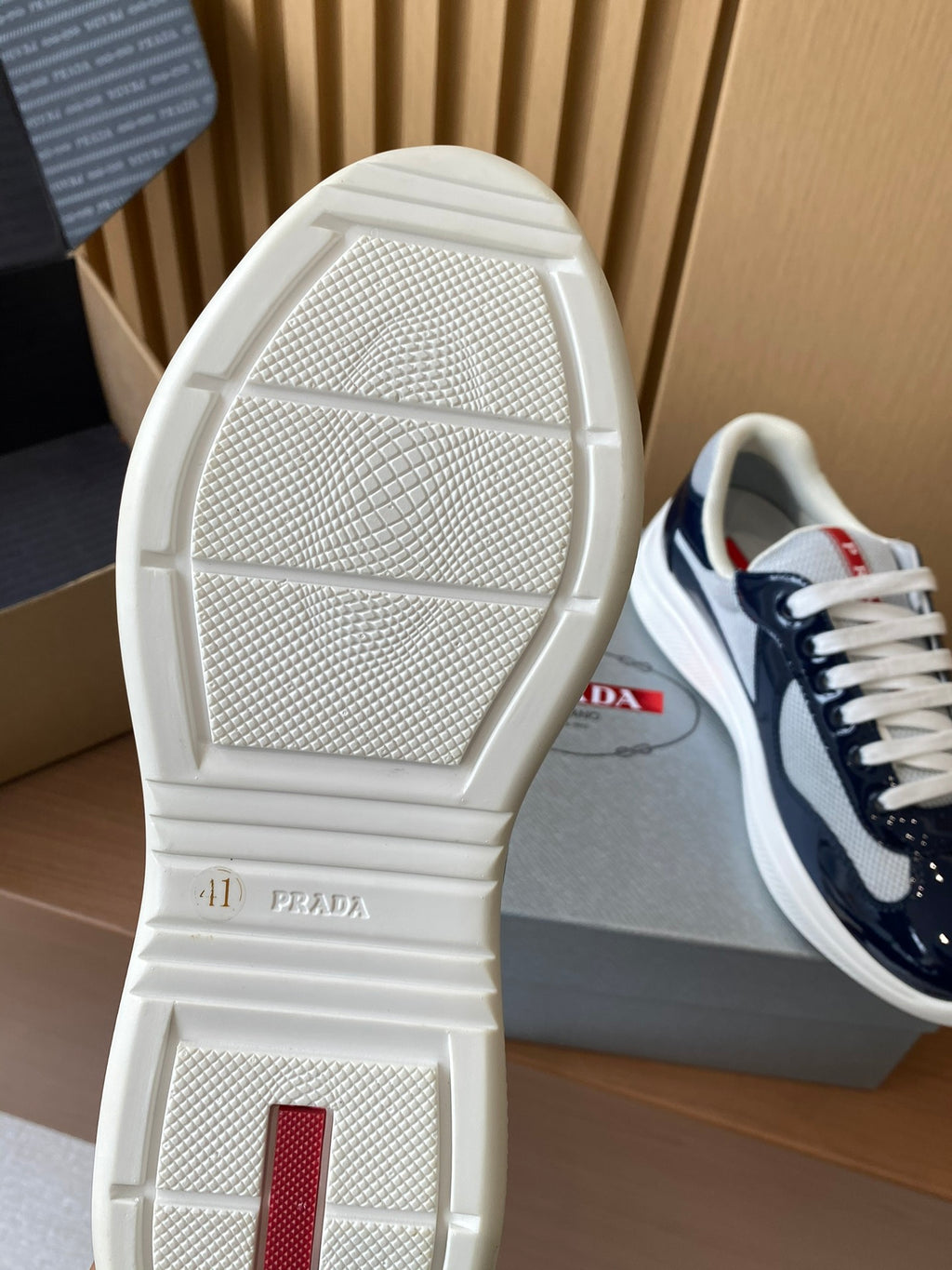 Prada sneaker outsole view in white with textured tread and red logo patch