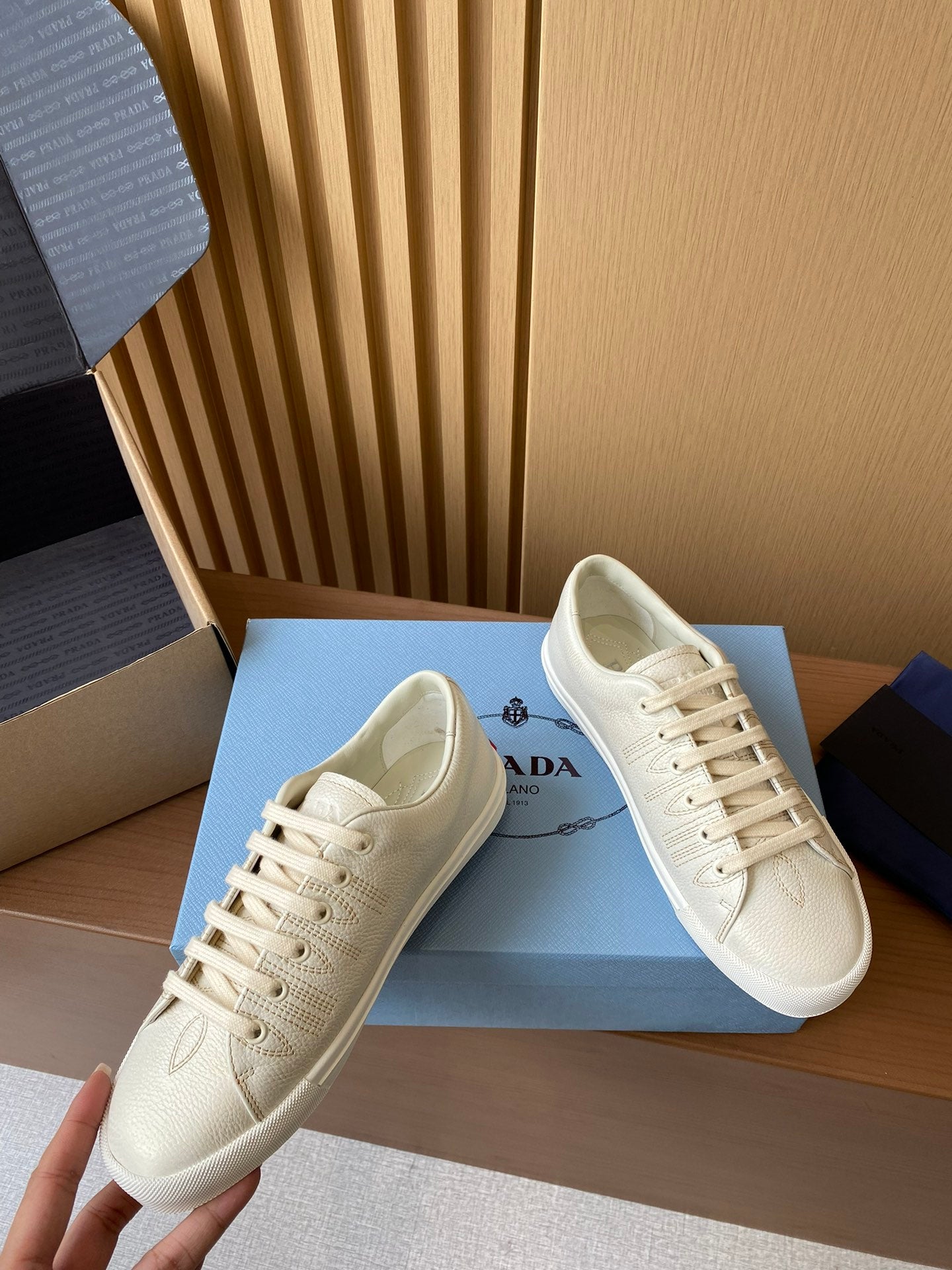 Prada unisex low-top sneakers, cream uppers with lace-up front and cushioned collar.