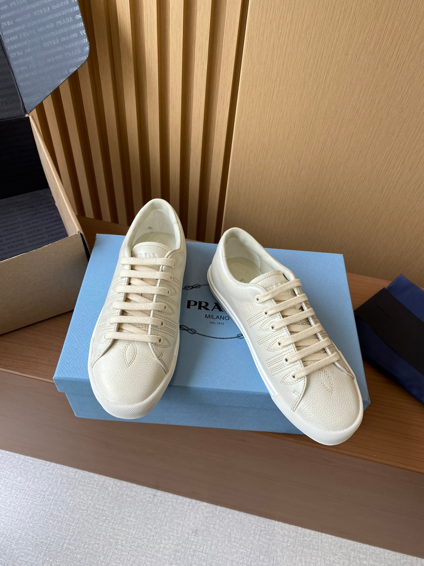 Prada unisex low-top sneakers, cream uppers with lace-up front and visible Prada logo detail.