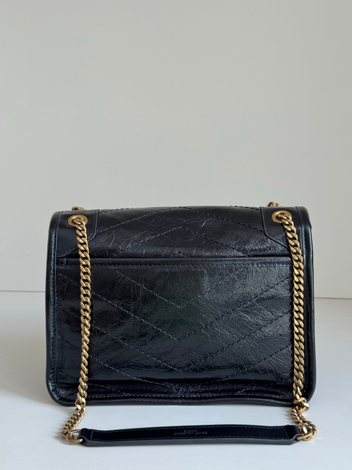 Black leather crossbody bag with flap, stitched design, and gold chain strap