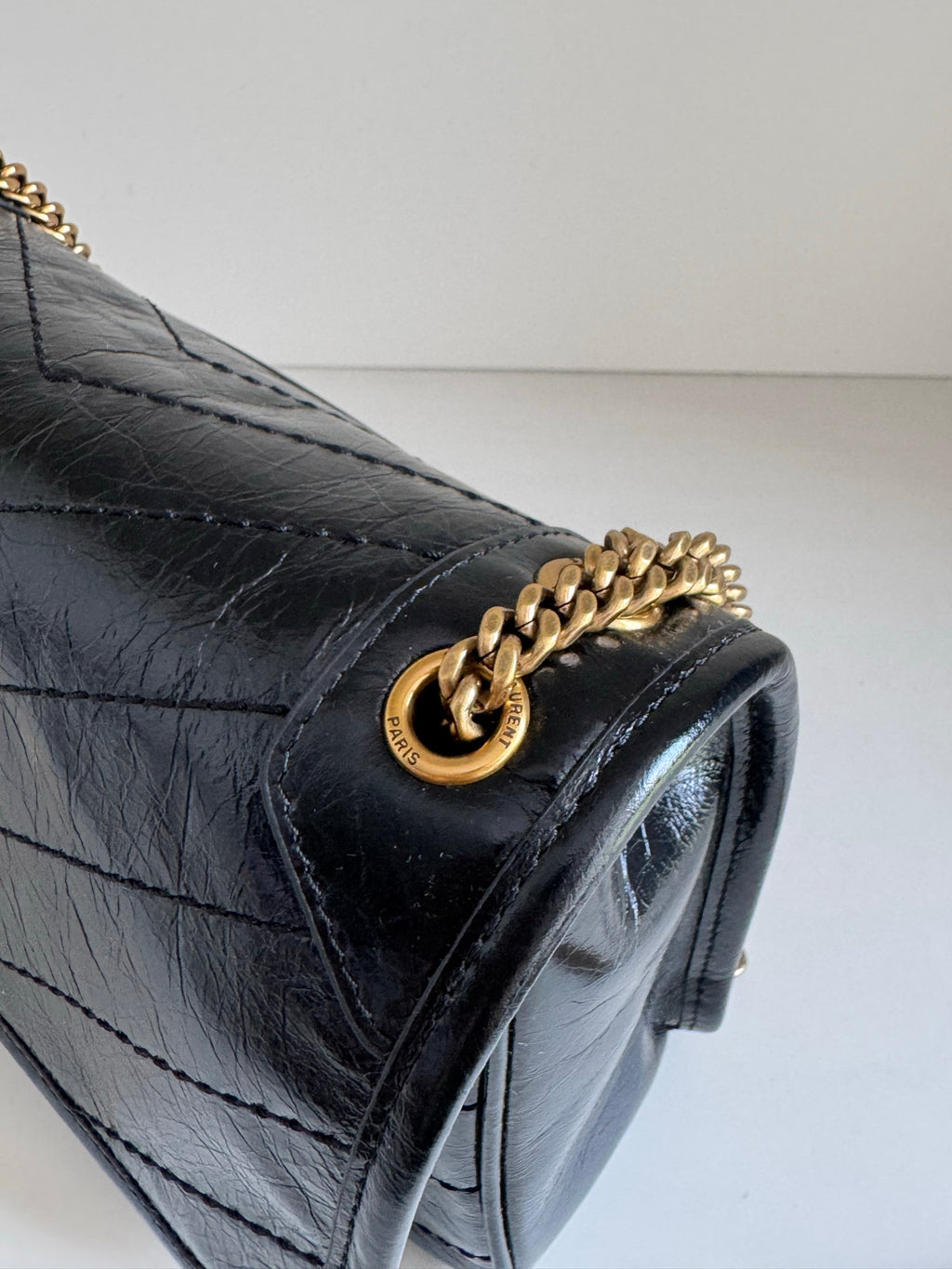 Black leather flap with gold chain shoulder detail and round logo clasp on corner