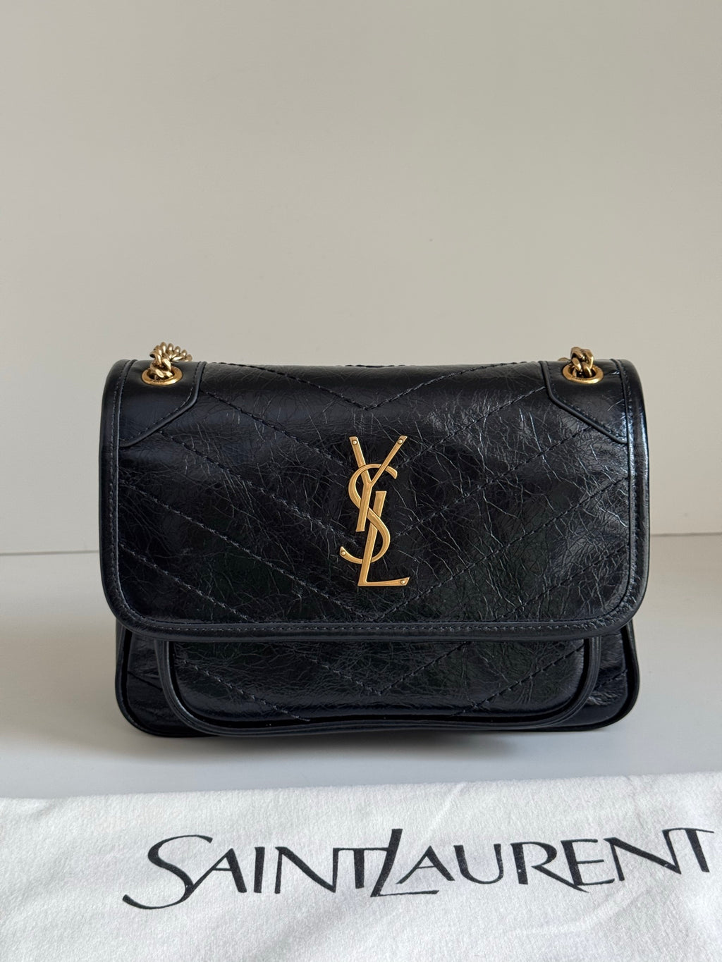 Black quilted leather shoulder bag with flap, gold YSL logo, and short chain handles