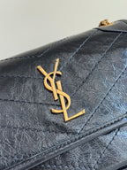 Black quilted leather flap with gold YSL logo, stitched panels, and chain corner detail