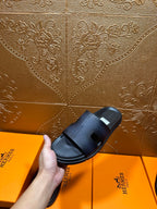 Hermes dark leather slide sandal held in hand, wide strap and open toe