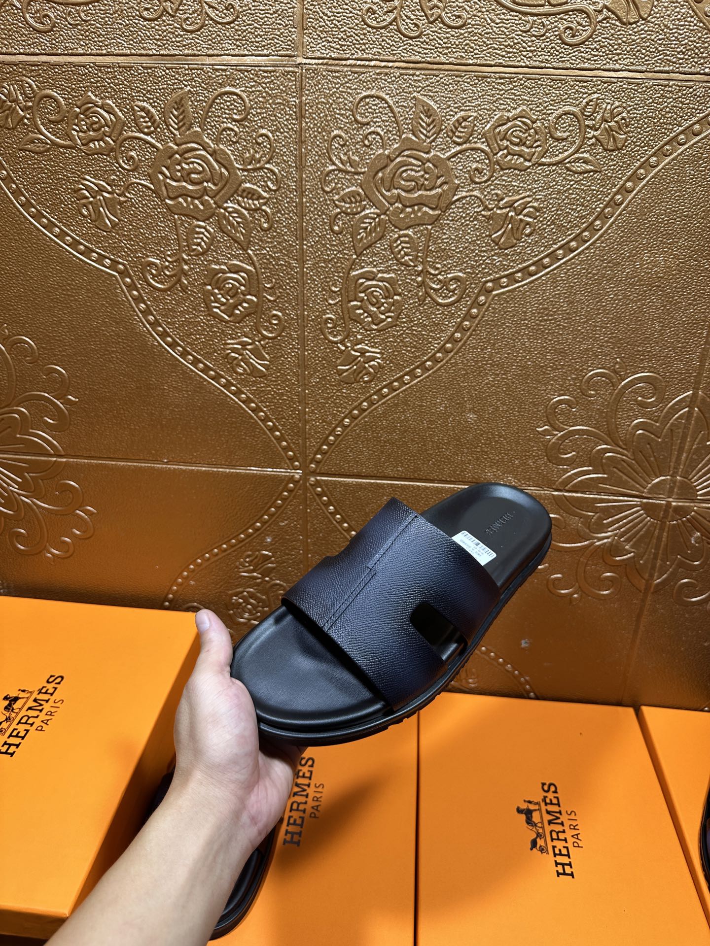 Hermes dark leather slide sandal held in hand, wide strap and open toe