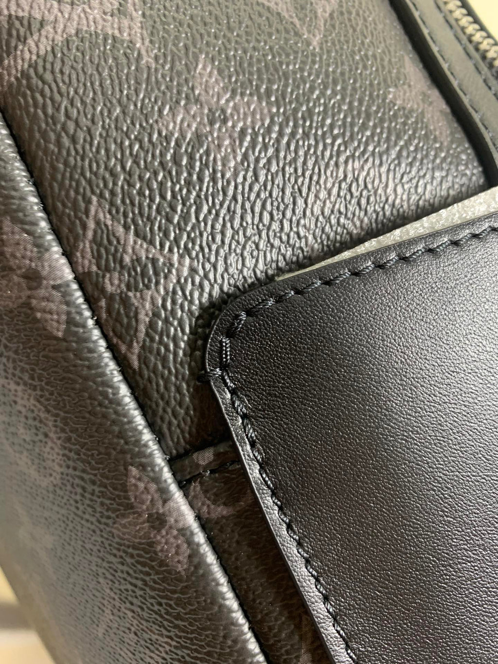 Monogram backpack close-up of textured leather trim and stitched zipper edge