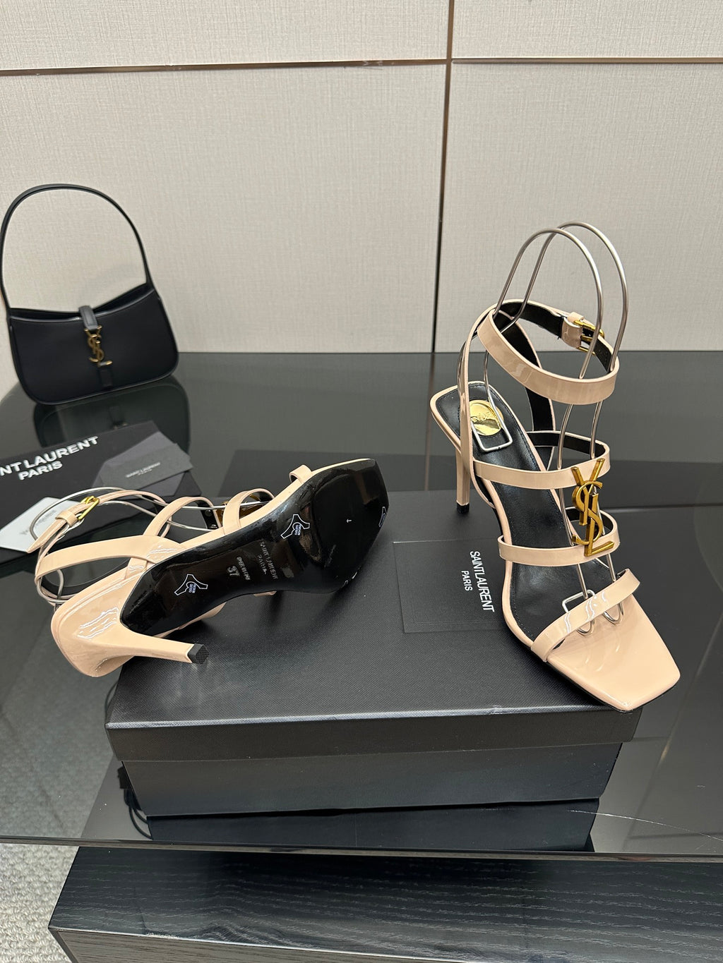 Beige strappy high-heel sandal with gold hardware, plus black clutch on display.