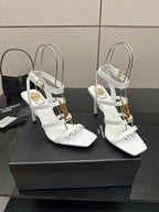 Pair of white high-heel sandals with gold-tone charms and open-toe, crisscross straps.